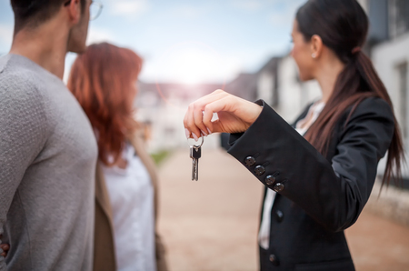 Keys hold by real estate agent with young couple of customers, copy spaceの写真素材