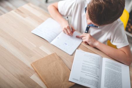 Focused preteen boy doing homework on desk in his room, copy spaceの写真素材