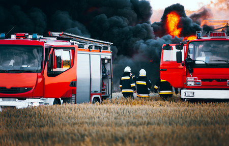 Red fire trucks in front of huge black smoke from the fireの写真素材