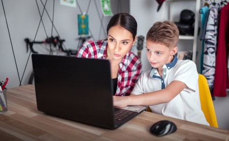 Mother and son using laptop in teenage room and spending time together at home