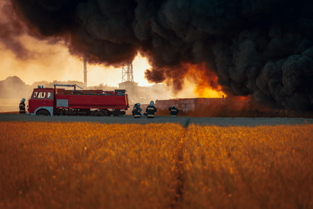 Firefighters with red truck in front of dark smoke from fireの写真素材