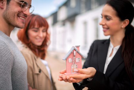 Model of house and keys hold by real estate agent with young couple of customers, copy spaceの写真素材