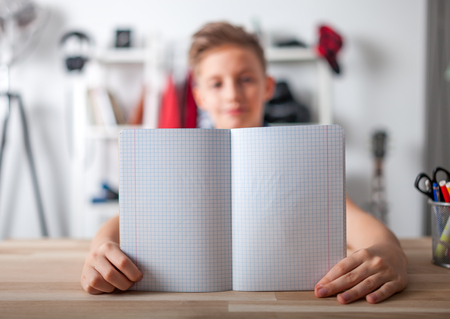 Kid boy in his room showing blank notebook, school conceptの写真素材