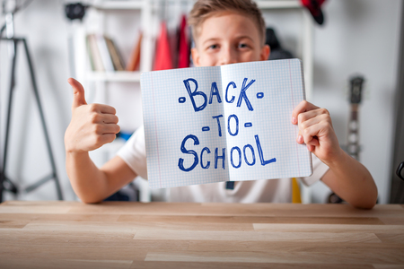Kid boy in his room showing blank notebook and giving thumbs up, school conceptの写真素材