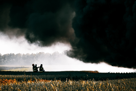 Firefighters standing under huge black cloud of smoke from the fireの写真素材