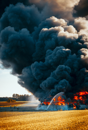 Firefighters with hose in front of huge fire among fieldsの写真素材