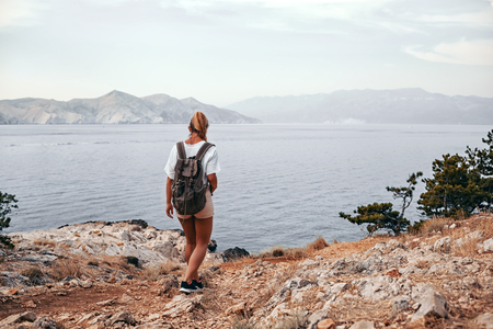 Hiker girl with backpack hiking on trail along sea bayの写真素材