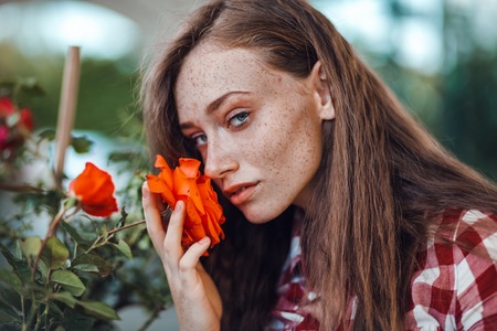 Beautiful freckled woman in checkered shirt smelling flower of rose, gardening conceptの写真素材