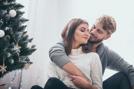 Couple celebrating Christmas together, sitting on floor next to Xmas treeの写真素材