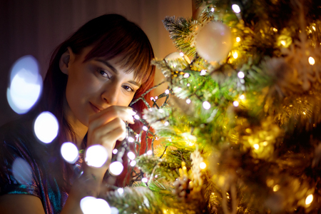 Young woman and Christmas tree full of lights decorationsの写真素材