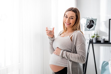 Health during pregnancy, Pregnant woman drinking water sitting on sofaの写真素材