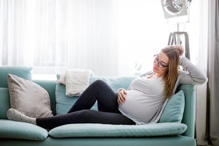 Young pregnant woman sitting on couch in living roomの写真素材
