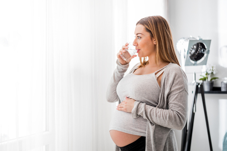 Health during pregnancy, Pregnant woman drinking water sitting on sofaの写真素材