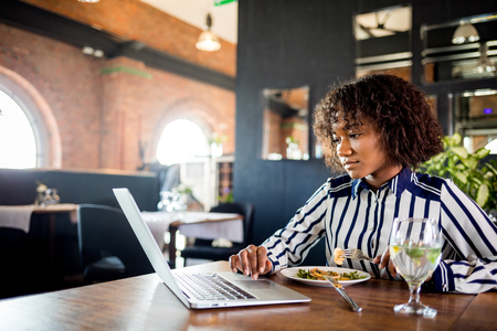 Focused black businesswoman using laptop in restaurantの写真素材