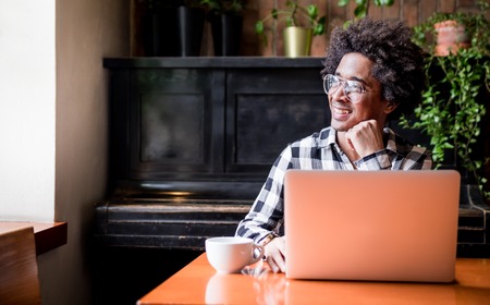 African man in glasses using laptop while sitting at restaurant, concept of young people working