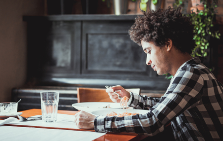 Young african american man eating lunch at restaurantの写真素材