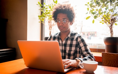 African man in glasses using laptop while sitting at restaurant, concept of young people workingの写真素材