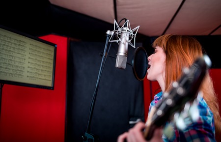 Young singer with guitar singing a song in recording studioの写真素材