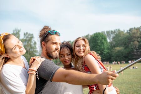 Friends at music festival taking live video to social media using smartphone on selfie stickの写真素材