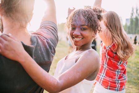 African American young woman covered in colorful powder with friends at holi festival