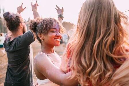 African American young woman covered in colorful powder with friends at holi festivalの写真素材