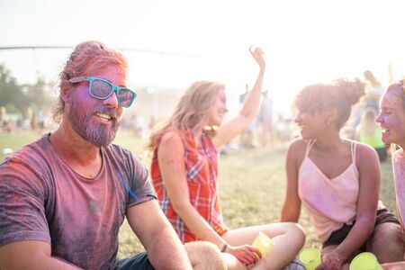 Friends sitting on grass and having fun at summer holi festival