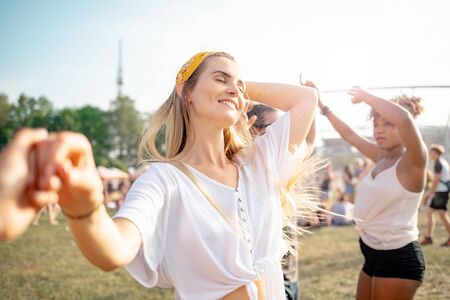 Beautiful young long haired woman dancing with friends outdoor at music festivalの写真素材