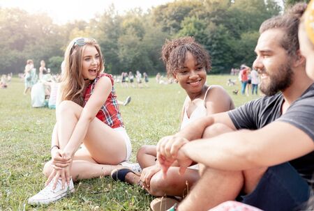 Friends sitting on grass and having fun at music festivalの写真素材