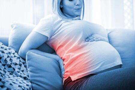Pregnant woman suffering from backache on sofa at home
