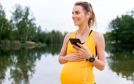 Pregnant woman using fitness app during exercises outdoorの写真素材