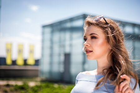 Elegant young woman walking around modern buildings and city garden on street