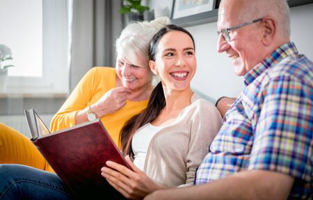 Senior couple with their daughter looking at photos in family album together