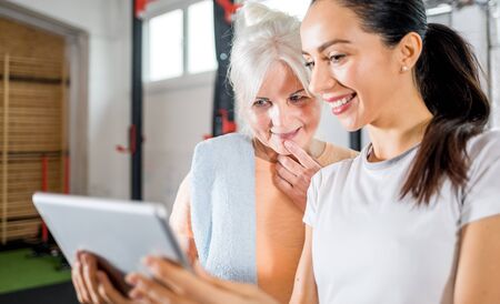 Trainer working with senior woman at the gym using tabletの写真素材