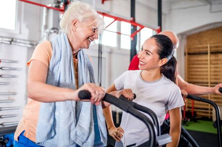 Senior woman biking at the gym with personal trainerの写真素材
