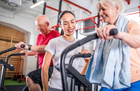 Senior couple biking at the gym with personal trainerの写真素材