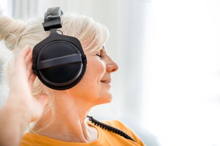 Relaxed senior woman listening her favourite music at home using big headphonesの写真素材
