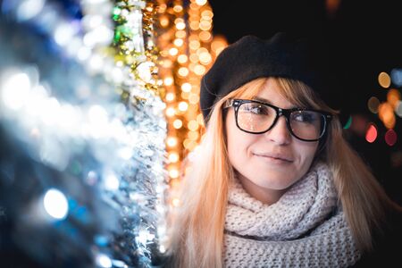 Happy smiling stylish woman walking on illuminated city street during Christmas nightの写真素材