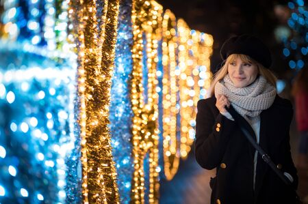 Young woman walking along illuminated alley during Christmasの写真素材