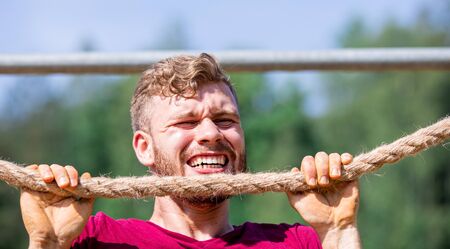 Fit man overcome obstacles using rope during extreme race in the boot camp