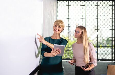Two business woman showing empty white board gives presentation at conference roomの写真素材
