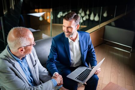 Younger and older businessman shaking hands in modern business loungeの写真素材