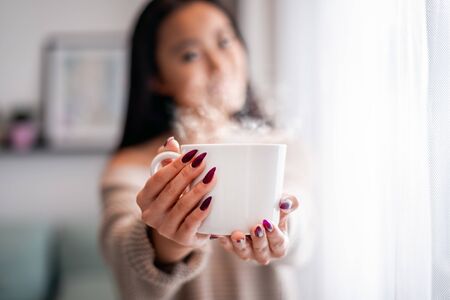 Cup of tea or coffee in hand of asian woman at home
