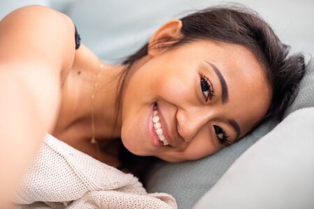 Smiling asian young woman laying in bed at homeの写真素材