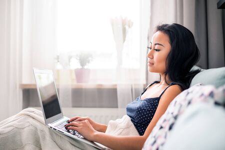Relaxed asian girl using laptop sitting on sofa at homeの写真素材
