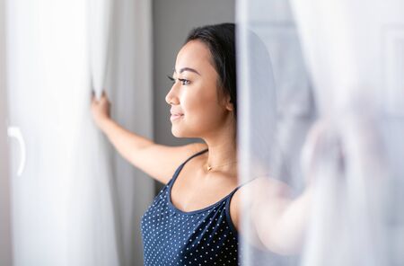 Asian girl wearing pajamas open window lace curtains in home at morningの写真素材