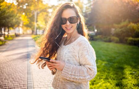 Cheerful long haired woman with mobile phone while walking on city streetの写真素材