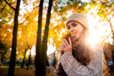 Outdoor lifestyle portrait of young woman with warm hat holding colorful autumn leaves and smilingの写真素材