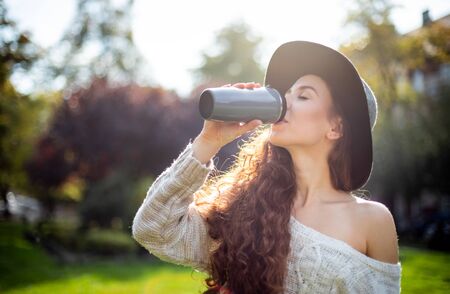 Stylish young woman walking in autumn city with thermo mug