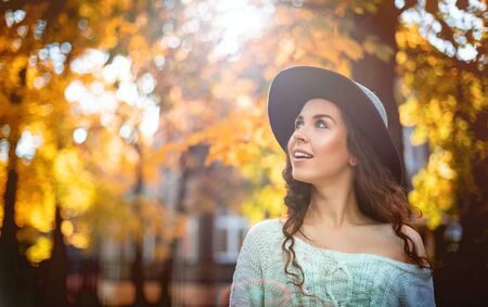 Pretty girl in hat standing on colorful autumn leaves background