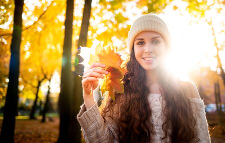 Outdoor lifestyle portrait of young woman with warm hat holding colorful autumn leaves and smilingの写真素材